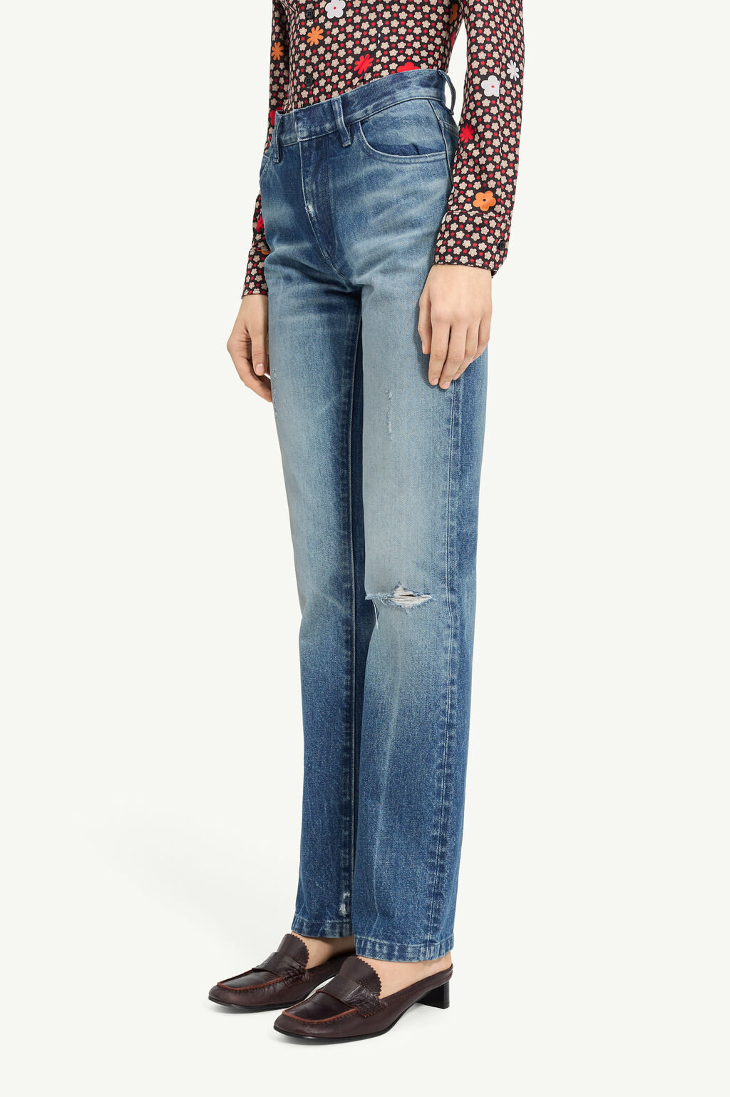 Person wearing high-waisted blue jeans with a ripped knee, a floral long-sleeve top, and brown loafers.