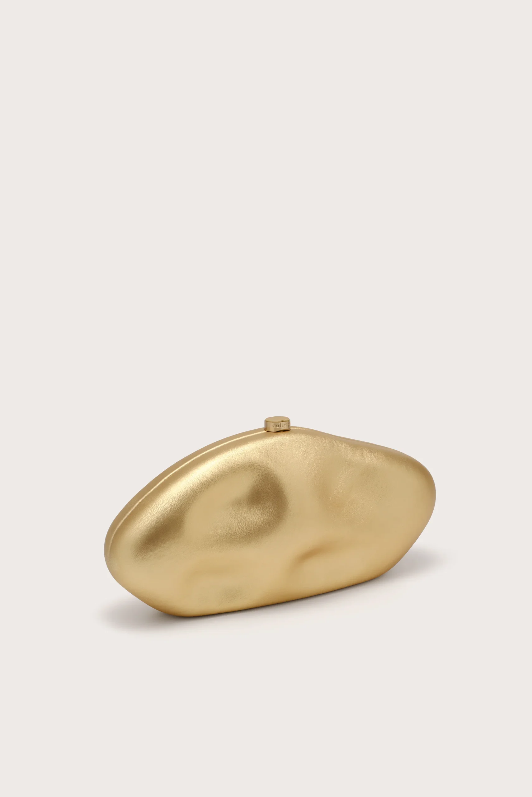 Gold metallic irregular pebble resting on a light beige background.