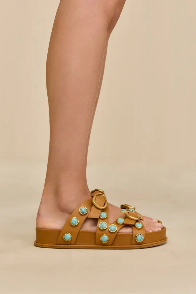 Side view of a foot in a tan platform sandal adorned with turquoise stones against a neutral background.