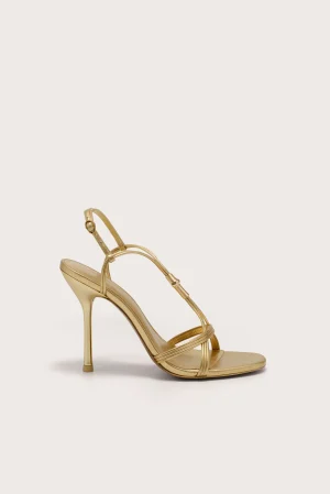Gold strappy high-heeled sandal shown from a side angle with stiletto heel on a light background, partial view of the shoe close to bottom left