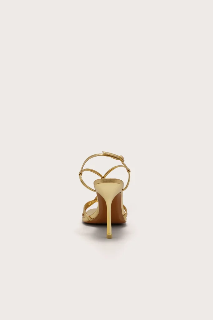 Back view of a gold metallic strappy high-heeled sandal on a white background, showing a tall stiletto heel and crisscross straps
