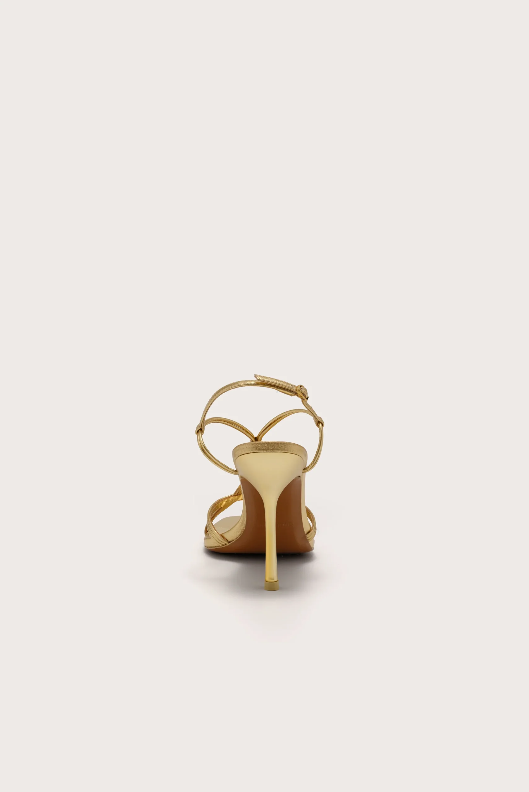 Back view of a gold metallic strappy high-heeled sandal on a white background, showing a tall stiletto heel and crisscross straps