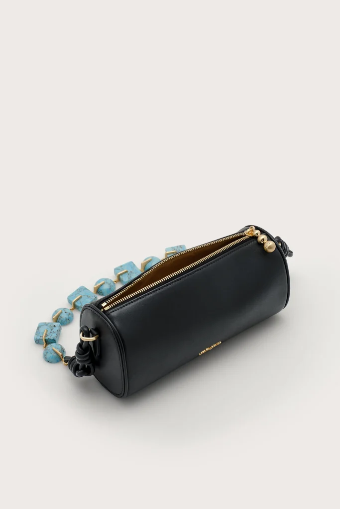 Black leather clutch with a gold zipper and turquoise bead strap on a light background
