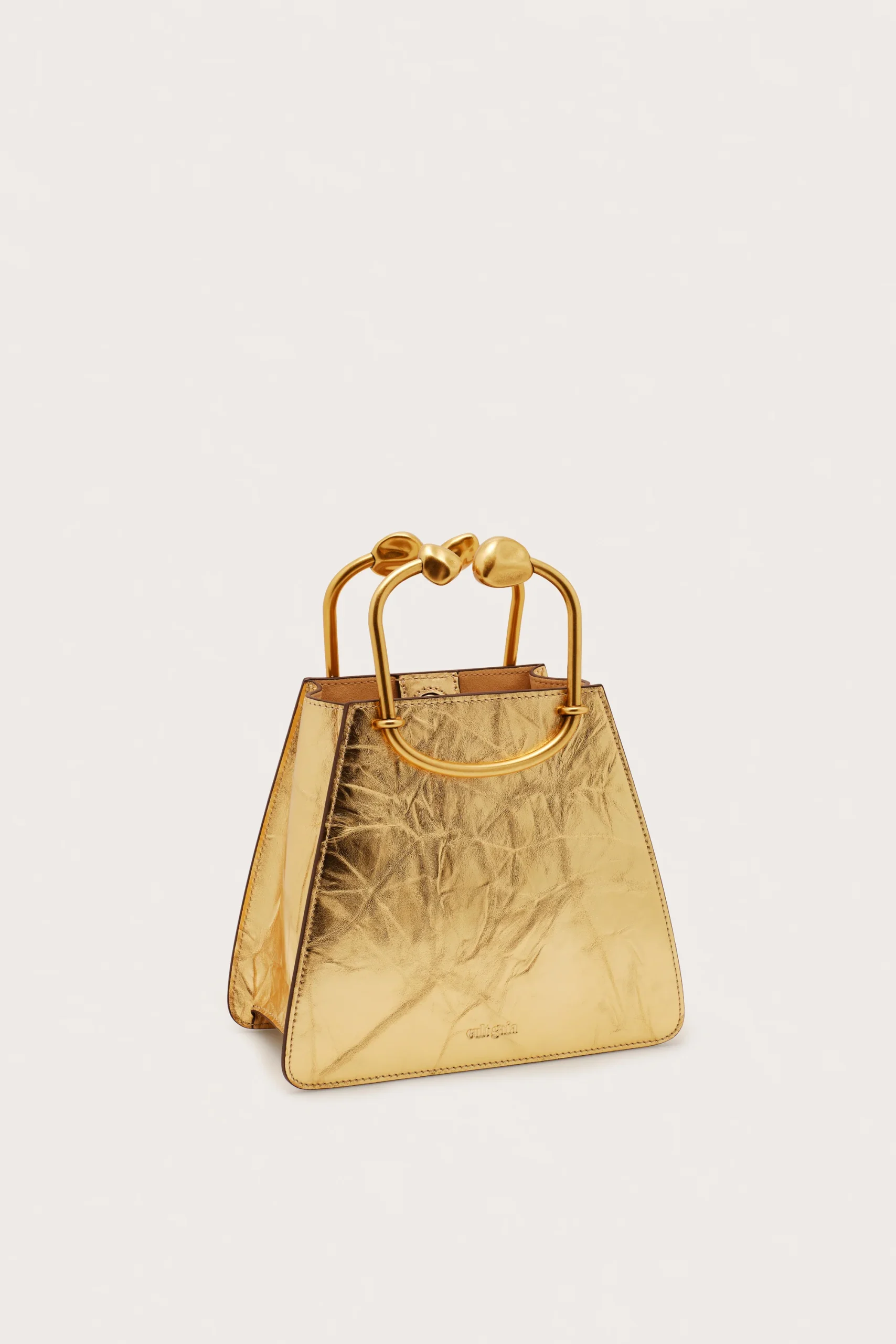 Gold metallic handbag with large rounded gold handles against a light background.