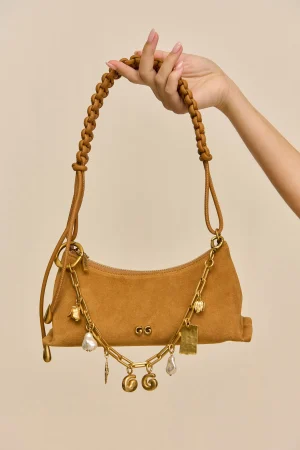 Tan leather handbag with a braided strap and gold chains being held up by a hand against a beige background.