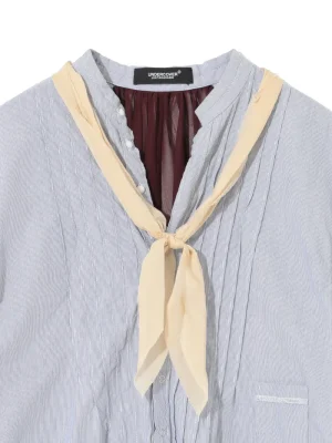 Light blue pinstriped button-down shirt with a cream neck scarf tied in a knot at the collar.