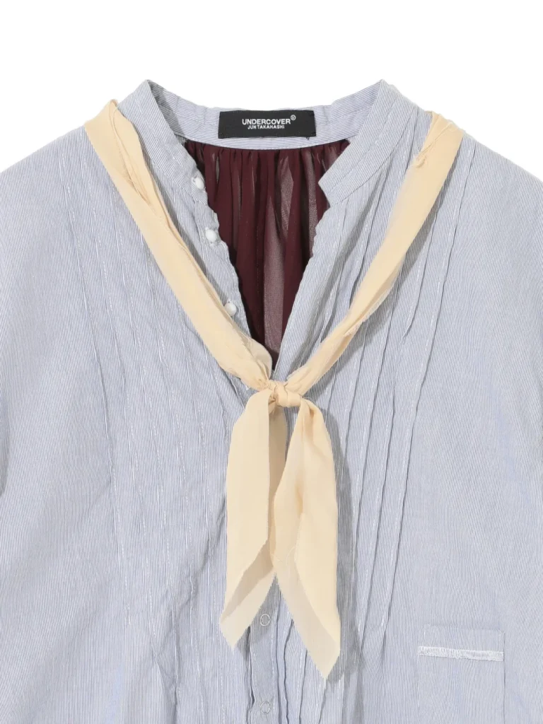 Light blue pinstriped button-down shirt with a cream neck scarf tied in a knot at the collar.