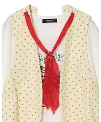 Beige polka-dotted sleeveless vest with a red scarf draped over a white printed shirt.