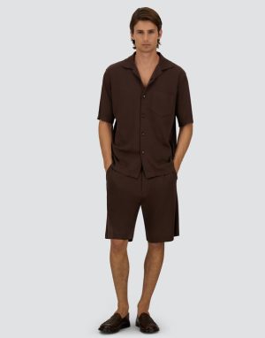 Male model wearing a dark brown matching short-sleeve button-up shirt with shorts and brown loafers, styled as a casual outfit.