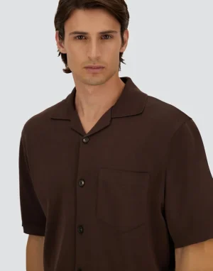 Male model wearing a brown short-sleeve button-up shirt with a front chest pocket, posing against a light gray background.
