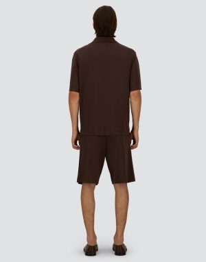 Man standing with his back to the camera, wearing a brown short-sleeve polo and matching shorts with brown sandals.