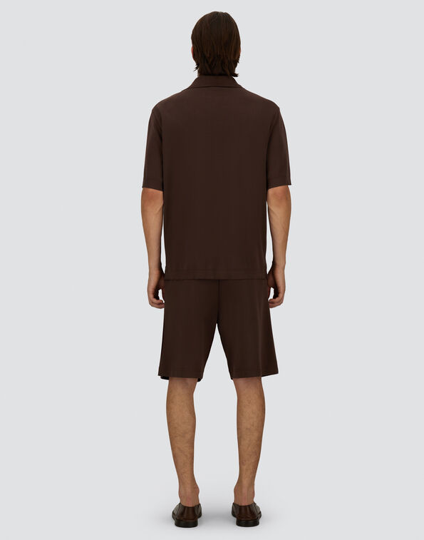 Man standing with his back to the camera, wearing a brown short-sleeve polo and matching shorts with brown sandals.