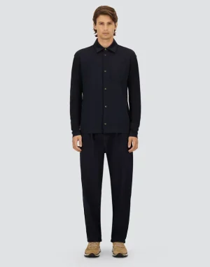 Full-body front view of a male model wearing a dark navy button-up shirt with a chest pocket and matching navy pants, beige sneakers.