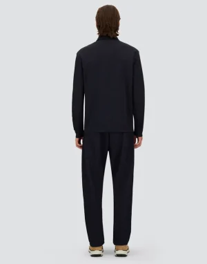 Back view of a person wearing a dark, long-sleeve jacket and matching loose dark pants, standing on a light gray background.