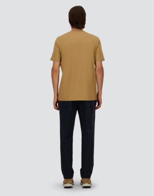Back view of a person wearing a tan short-sleeve T-shirt, dark jeans, and tan sneakers against a light gray background.