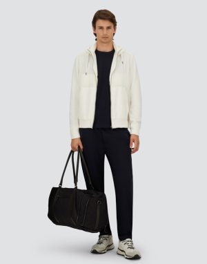 Man wearing a cream zip-up jacket over a navy T-shirt and navy trousers, holding a black duffel bag.