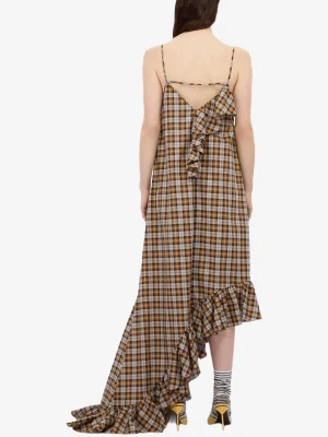 Back view of a model wearing a brown plaid sleeveless dress with thin straps and a triangular open back, featuring a cascading ruffle and a long, asymmetrical hem.