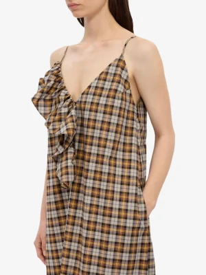 Model wearing a brown plaid dress with thin straps and a large ruffle detail along the neckline on one side.