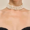 Triple-strand white pearl necklace around a model’s neck with a black off-shoulder top.