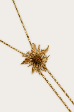 Gold chain necklace with a large ornate floral pendant against a pale background.