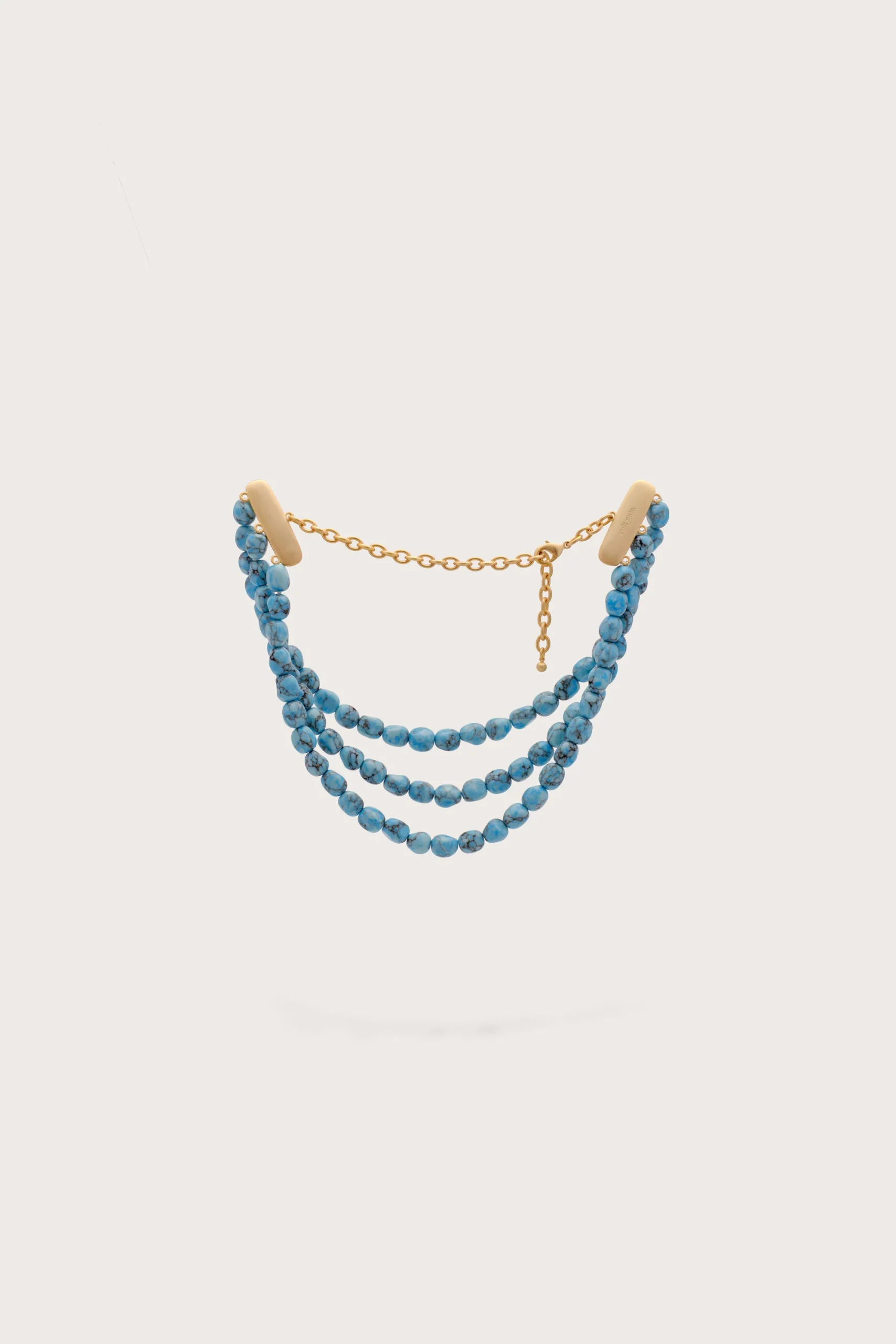Turquoise bead multi-strand necklace with gold chain accents on a pale background.