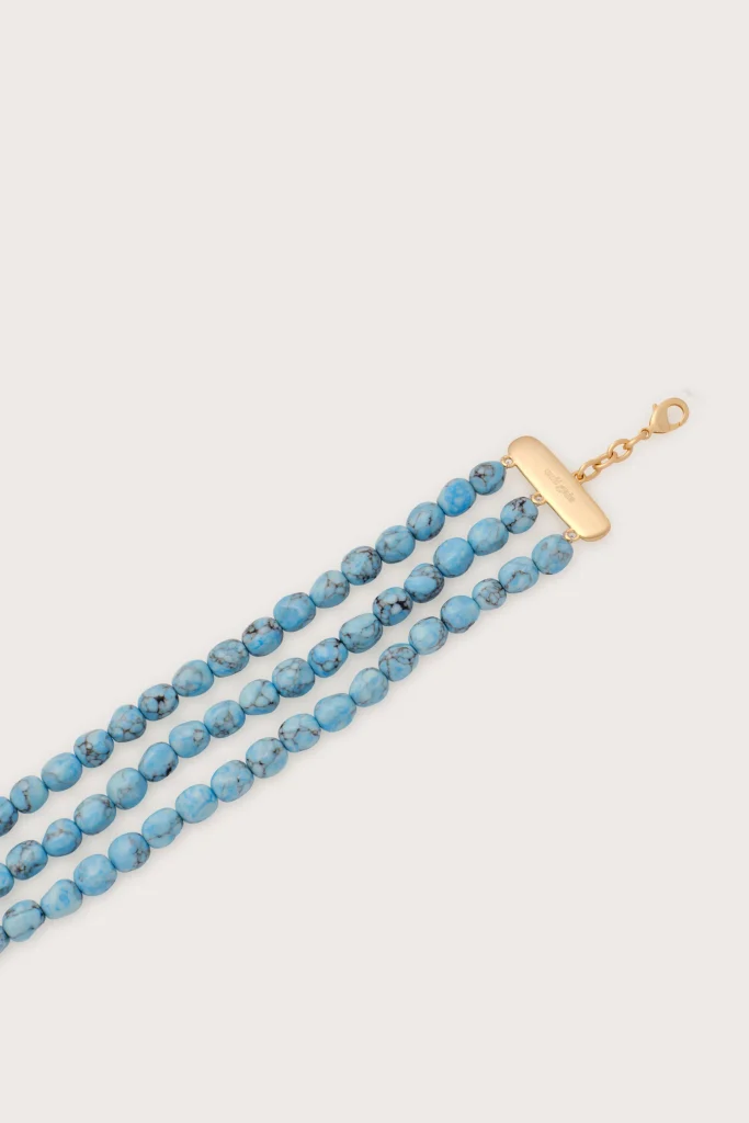 Turquoise beaded necklace with a gold rectangular clasp on a pale background, worn diagonally across the image.