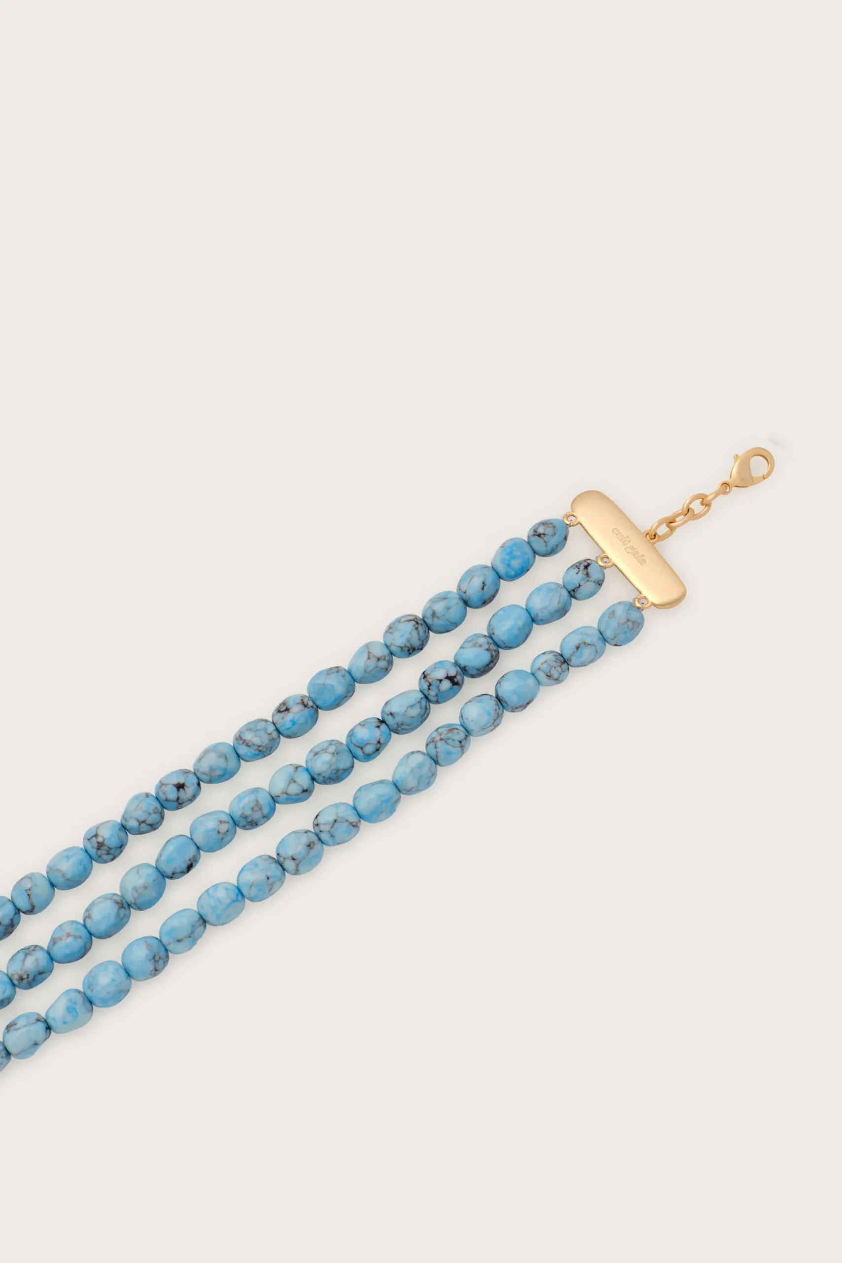 Turquoise beaded necklace with a gold rectangular clasp on a pale background, worn diagonally across the image.