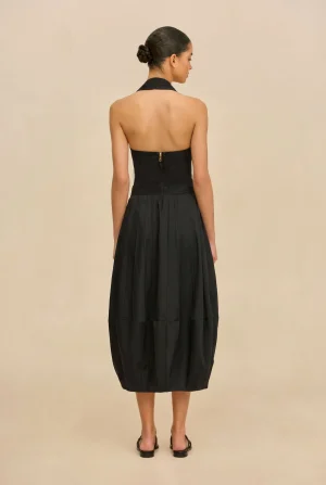 Back view of a woman in a black halter-neck dress with a zipper at the back and a pleated skirt, her hair in a bun.