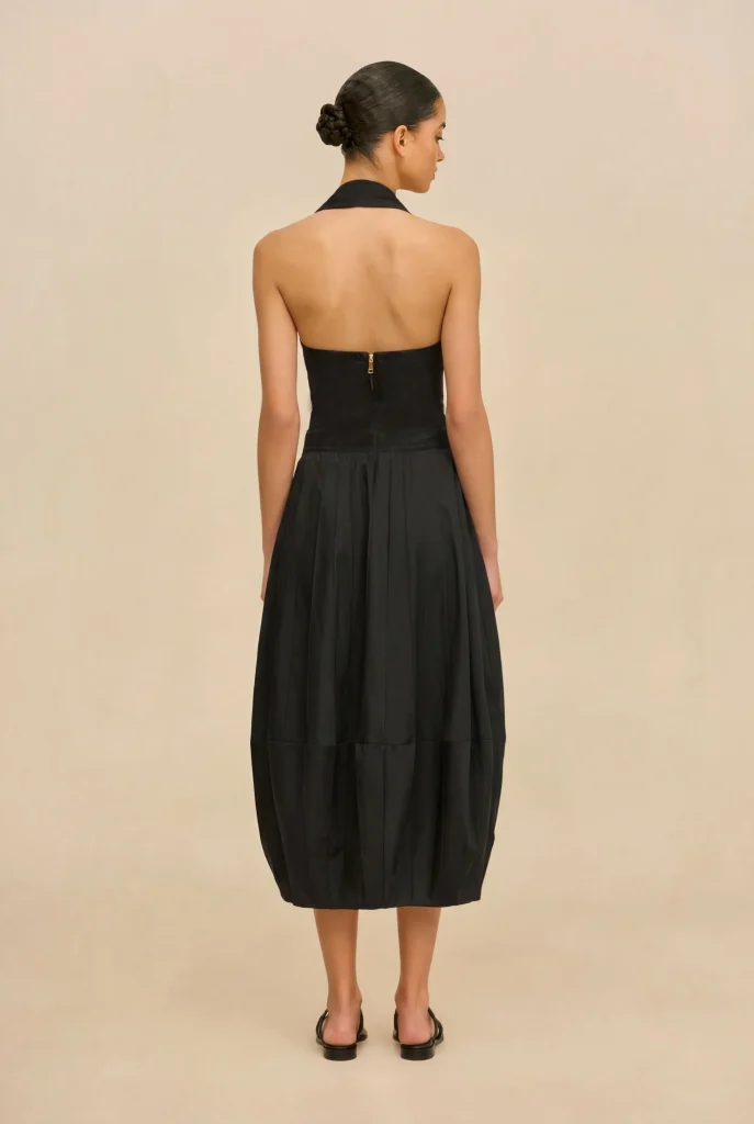 Back view of a woman in a black halter-neck dress with a zipper at the back and a pleated skirt, her hair in a bun.