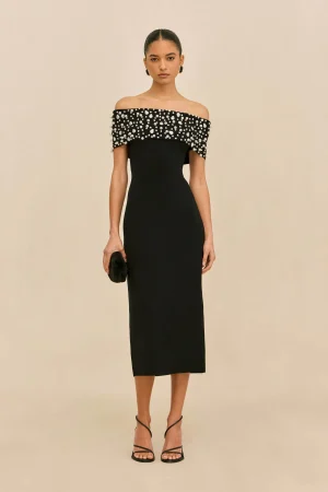 Slender woman wearing an off-shoulder black evening gown with a beaded, pearl-studded bodice, holding a small black clutch.