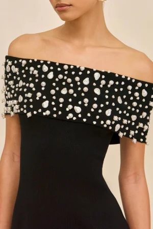 Close-up of a woman's off-the-shoulder black dress decorated with scattered white pearl beads along the neckline.