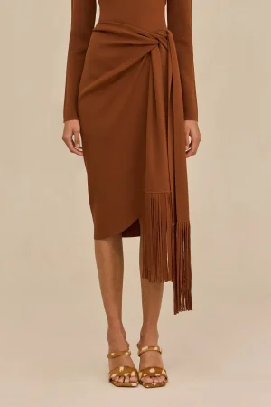 Rust-brown wrap dress with a tied waist and long fringe tassels, paired with tan sandals.