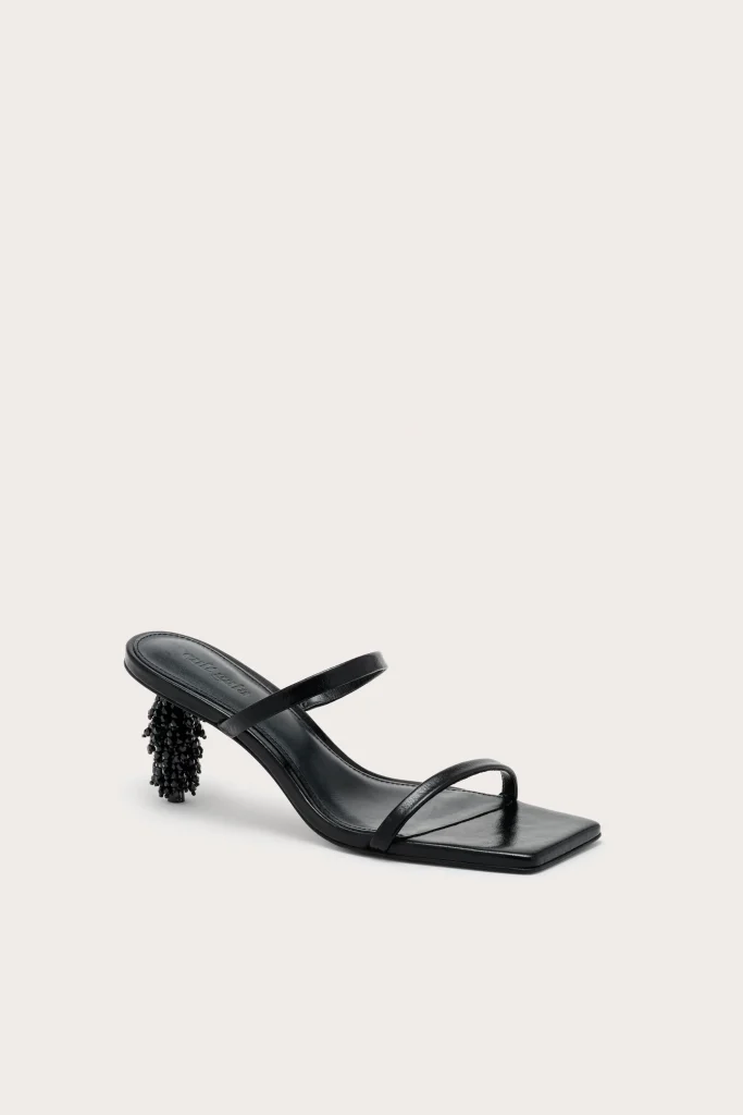 Black open-toe heeled sandal with a beaded cylindrical heel on a pale backdrop.