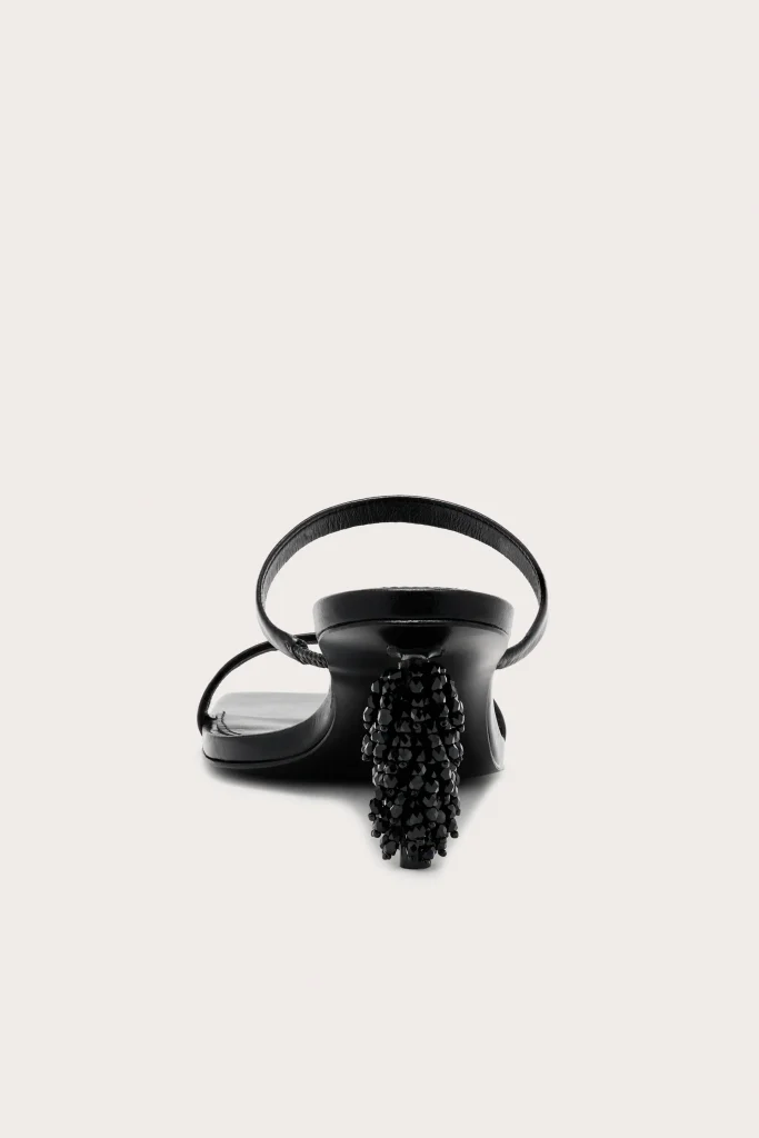 Black strappy sandal with a high beaded heel, pictured against a pale background.