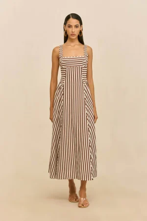 Full-length model wearing a brown-and-white vertical striped maxi dress with a squared neckline and large gold hoop earrings, standing against a beige backdrop.