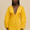 Woman wearing a bright yellow dress with a deep V-neck and twisted front detail against a beige background.