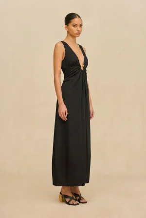 Full-length black evening gown with a plunging V-neck and gathered waist accent at the center, worn by a model in a studio setting.