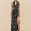 Model wearing a navy blue halter maxi dress with white polka dots and a front slit, standing against a beige backdrop.