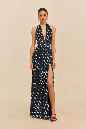 Model wearing a navy blue halter maxi dress with white polka dots and a front slit, standing against a beige backdrop.