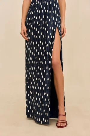 Navy blue maxi dress with white polka dots and a tall side slit revealing part of the leg, paired with red strappy sandals.
