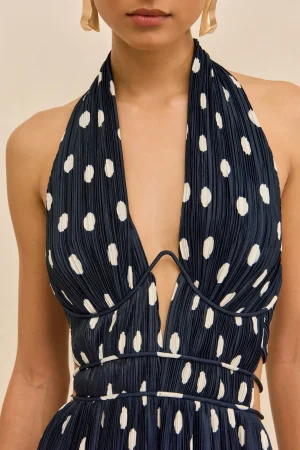 Close-up of a woman wearing a navy halter dress with white polka dots and pleated fabric.