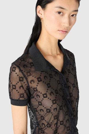 Close-up of a woman wearing a sheer black patterned blouse with a black collar and small hoop earring in the ear.