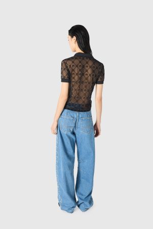Back view of a person wearing a sheer black lace short-sleeve top and blue jeans against a light gray background.