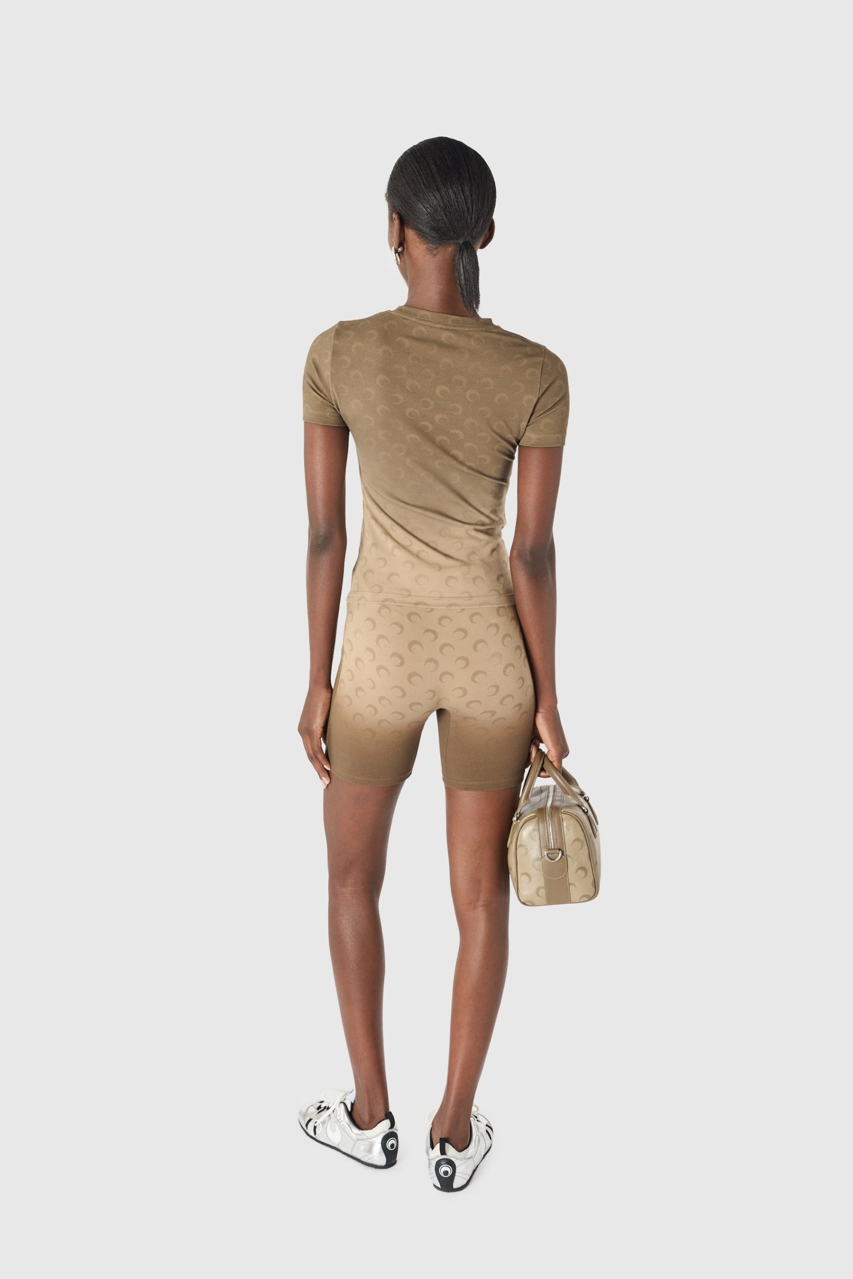 Back view of a person in a tan matching athletic set with a patterned texture, holding a beige handbag