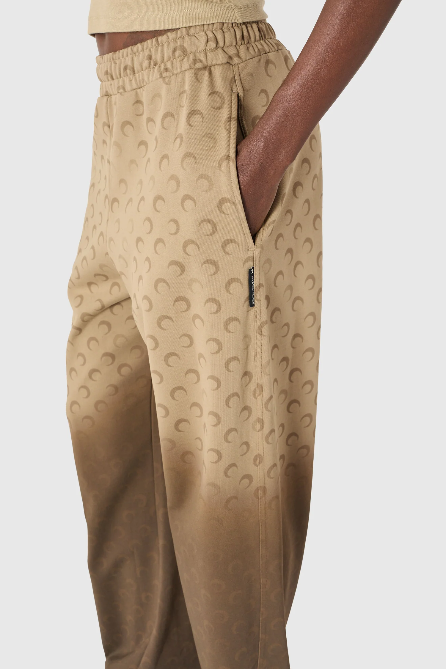 Beige jogger pants with an elastic waistband and a crescent pattern, showing a side pocket.
