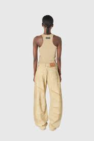 Back view of a person wearing a beige sleeveless top and loose beige pants, standing with arms at sides.