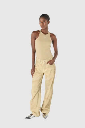 Full-body shot of a woman wearing a beige tank top and matching beige cargo pants, standing with one hand in pocket against a light gray background.