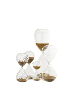 Stacked assortment of clear glass hourglasses with brown sand on a white background.